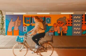 a woman riding a bike in front of a colorful wall - Citymarketing Eindhoven door Peter kentie